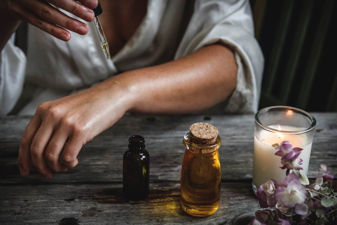 woman applying aromatic oil to her forearm with a candle on the table